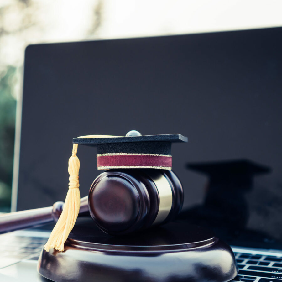 image: A gavel sits on top of a laptop with a small graduation cap on top of it