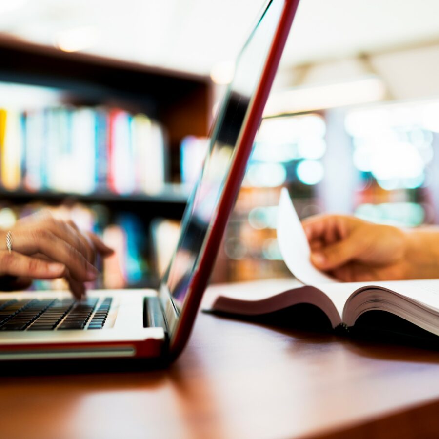 Image: Out of focus photo of someone typing on a laptop computer and another person reading a book